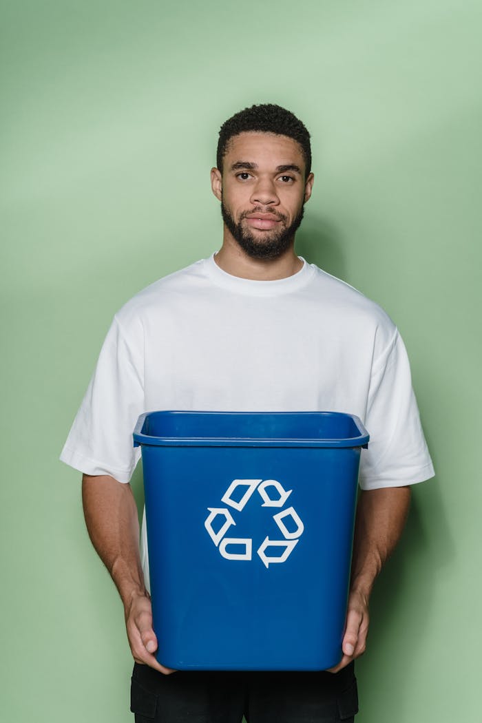 Portrait of a young man holding a blue recycling bin, emphasizing sustainability and eco-friendly initiatives.